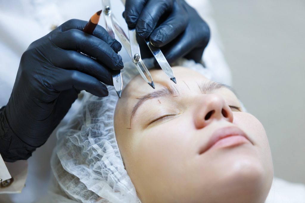 Microblading eyebow artist mapping client eyebrows to determine best brow shape face